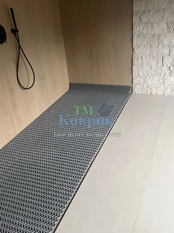 Shower area with a dark metal anti-slip grate mat running along the floor and a handheld shower hose mounted on the wall to the left.